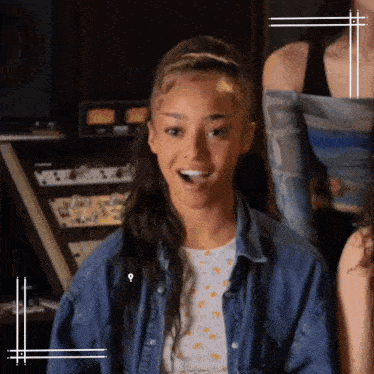 a woman in a denim shirt is smiling and looking at the camera while standing in a room .