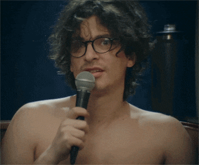 a shirtless man with glasses is holding a microphone in his hand