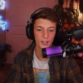 a young man wearing headphones and a plaid shirt is talking into a purple microphone .