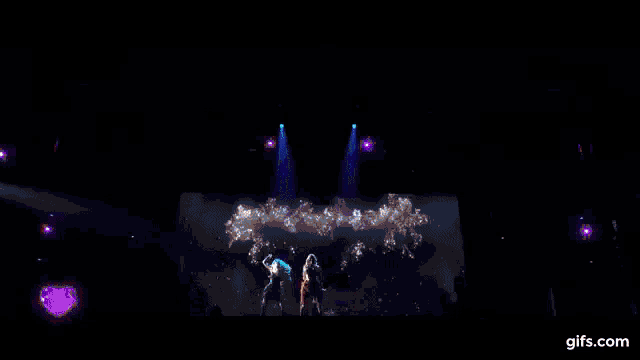 a woman is singing into a microphone on a stage in front of a large screen .