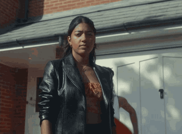 a woman in a black leather jacket stands in front of a brick wall