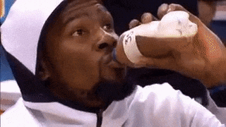 a man is drinking milk from a bottle while wearing a white hooded jacket .