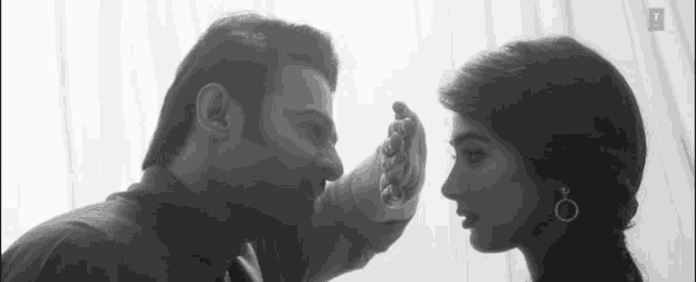a black and white photo of a man and a woman looking at each other .