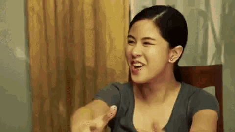a woman is sitting in a chair making a funny face and pointing .