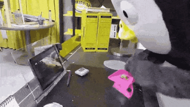 a stuffed animal is sitting at a table with a tablet and a notebook .