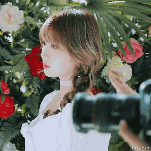a woman in a white dress is being photographed by a camera while standing in front of flowers .