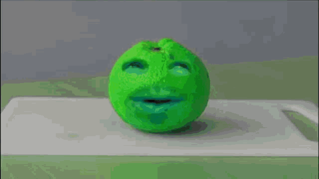 a green toy with a face on it is being smashed by a hammer on a cutting board .