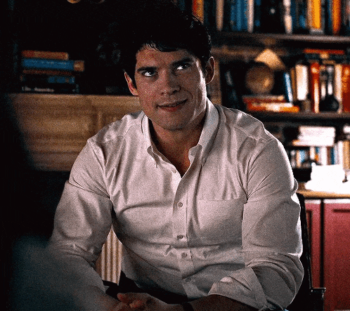 a man in a white shirt is sitting at a table in front of a bookshelf .