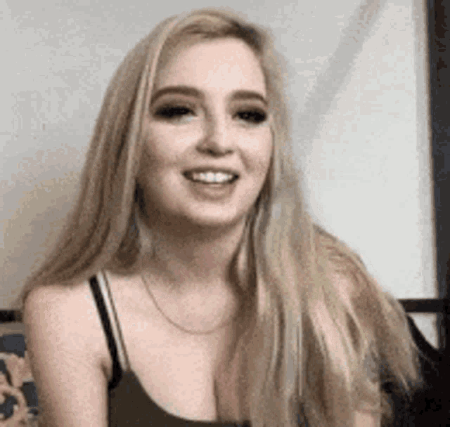 a woman with long blonde hair is smiling while sitting on a couch .