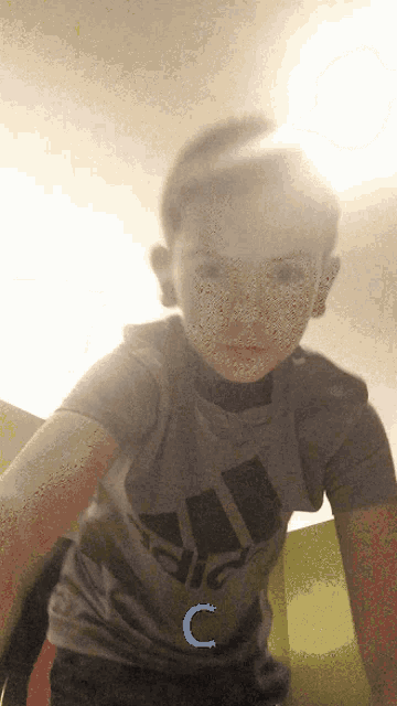 a young boy wearing a grey adidas shirt with the letter c on it
