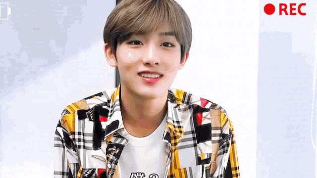 a young man in a plaid shirt is smiling in front of a red rec button