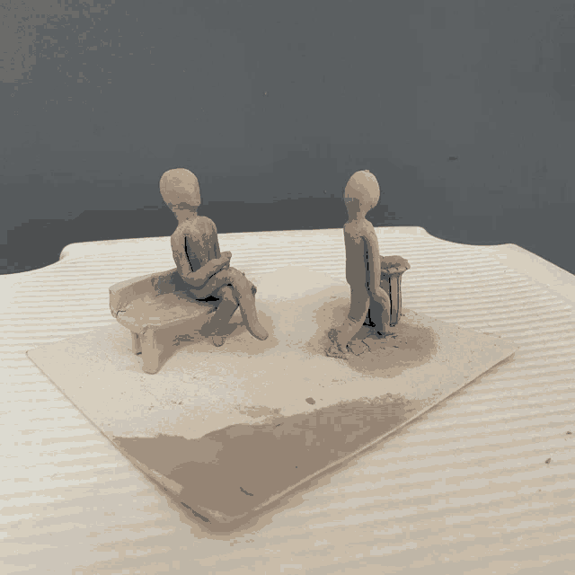 a clay sculpture of a man sitting on a bench and a clay sculpture of a man standing on a bench
