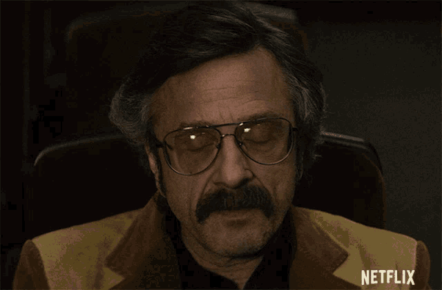 a man with glasses and a mustache is sitting in a netflix chair