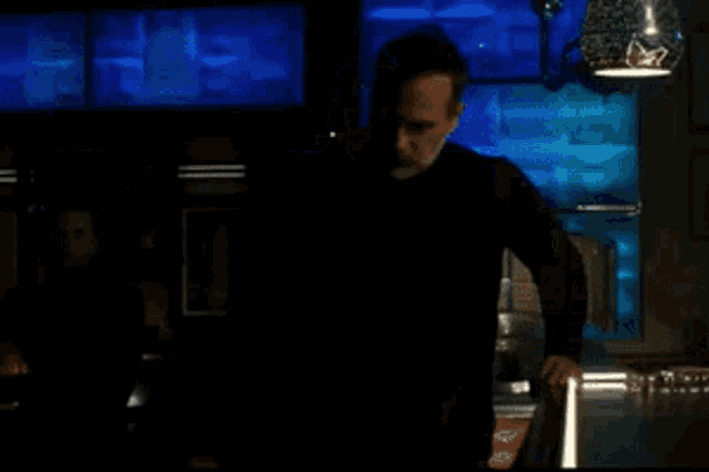 a man in a black turtleneck stands in front of a blue wall and says but uh speaking of harrowing stories