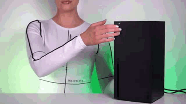 a woman in a white shirt is standing next to a black xbox console .