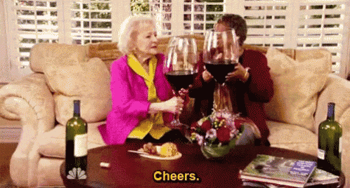 two older women are sitting on a couch holding glasses of wine .