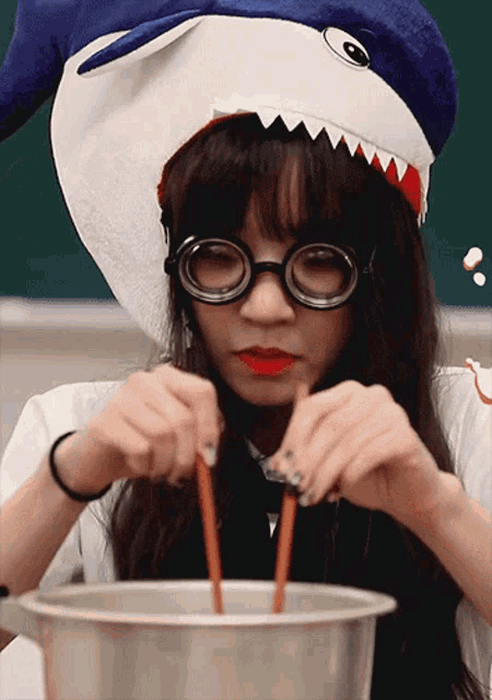 a girl wearing a shark hat and glasses is stirring something in a bowl