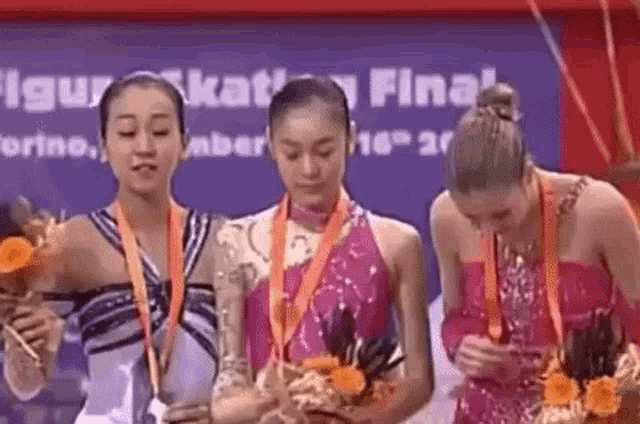 three female gymnasts are standing next to each other holding medals and flowers .
