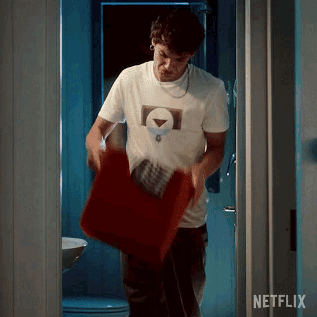 a man in a white t-shirt is carrying a red bag with a netflix logo on the door