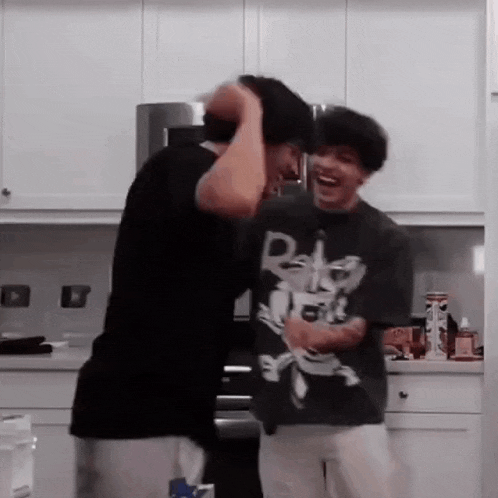 two men are standing next to each other in a kitchen laughing .