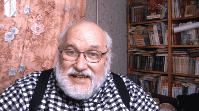 a man wearing glasses and a plaid shirt stands in front of a bookshelf with russian books