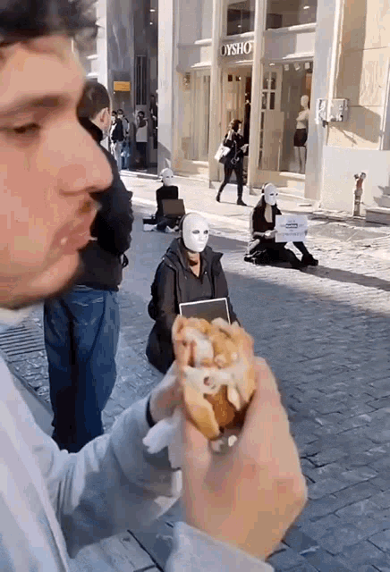 a man is eating a sandwich in front of a store that says dysho