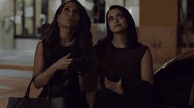 two women are standing next to each other and one is holding a black purse