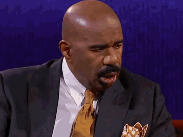 a bald man in a suit and tie is laughing while holding a glass of water .