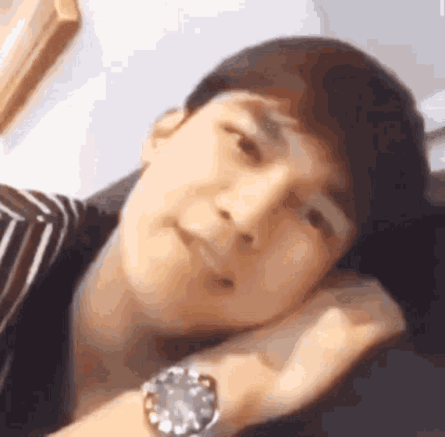 a man wearing a watch is laying on a couch with his head on his arm .