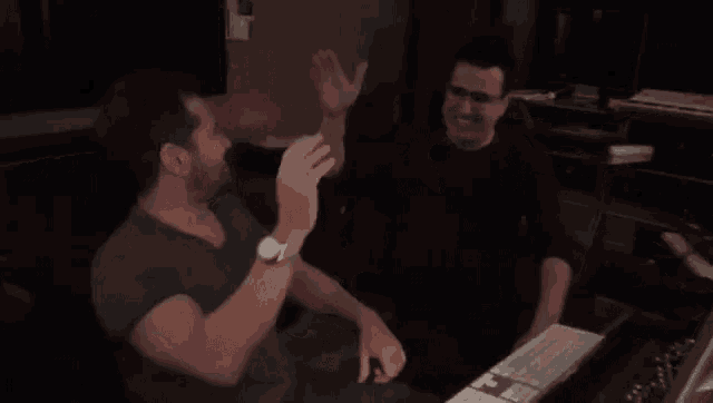 two men are giving each other a high five while sitting in front of a keyboard