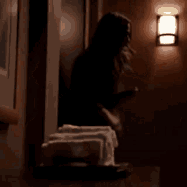 a woman is standing in a dark hallway next to a lamp .