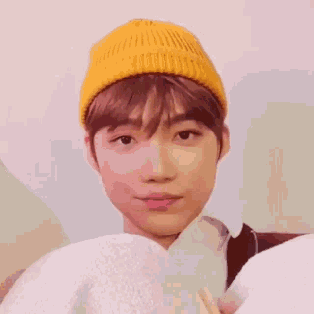 a young man wearing a yellow beanie is sitting on a couch and making a funny face .