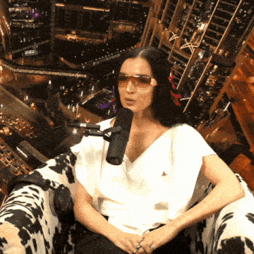 a woman wearing sunglasses is sitting in front of a microphone in a cow print chair