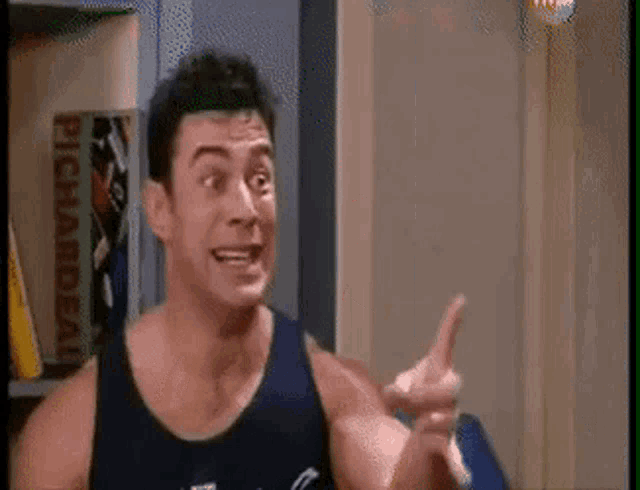 a man in a tank top is making a funny face and pointing at the camera .