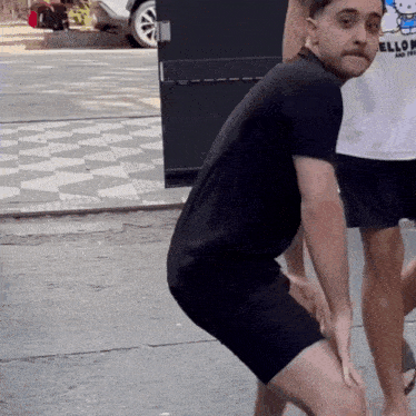 a man wearing a hello kitty shirt is squatting down on the street