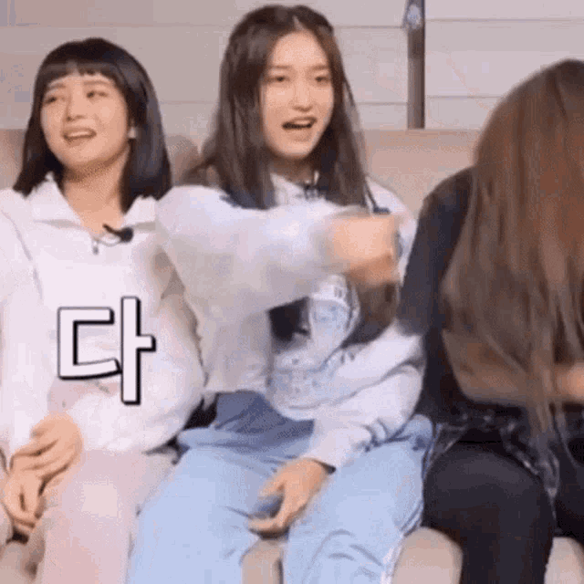 a group of young girls are sitting on a couch and one of them is pointing at the camera .