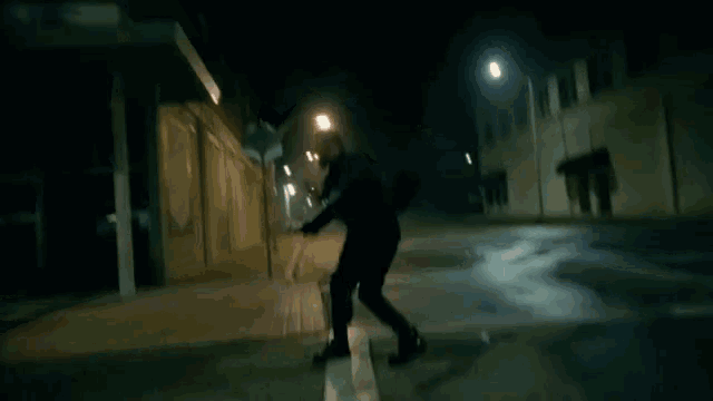 a man in a black suit is walking down a dark street at night