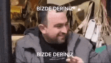 a man is sitting at a table in front of a window with a sign that says `` bizde deriniz '' .
