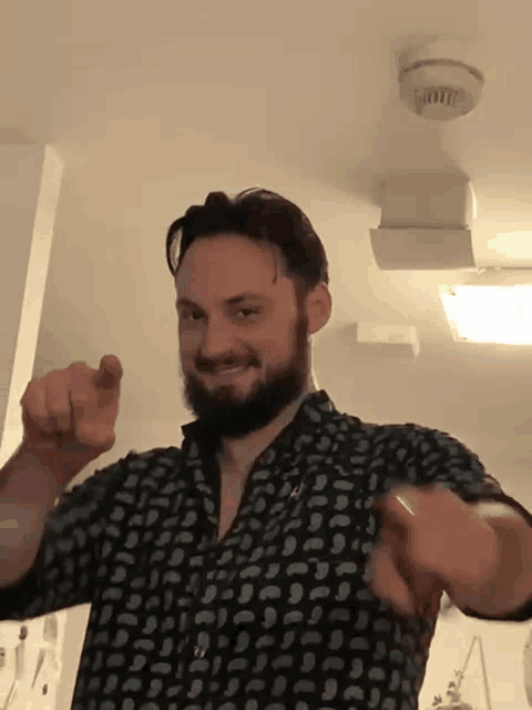 a man with a beard wearing a black shirt is pointing at the camera