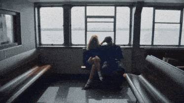 a man and a woman sit on a bench in front of a window