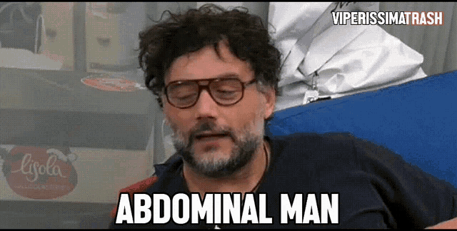 a man with glasses and a beard is laying on a bed and says abdominal man