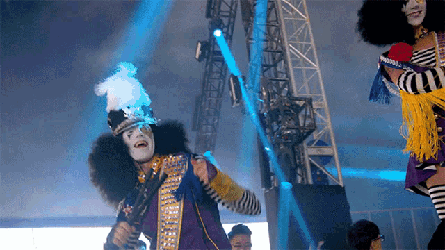 a man in a clown costume is playing a guitar in front of a blue light