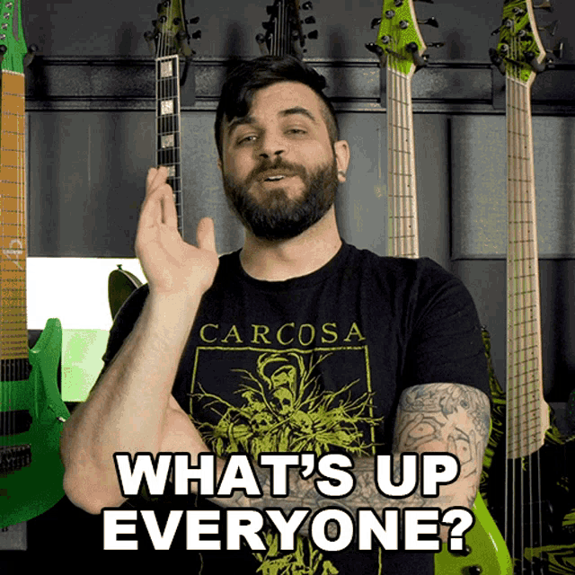a man with a beard wearing a carcosa shirt says " what 's up everyone "
