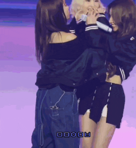 three women are hugging each other on a stage with the letters aooo on the bottom right