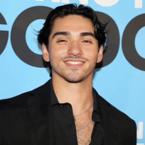 a man wearing a black shirt and a black jacket smiles in front of a blue background with the letter o on it