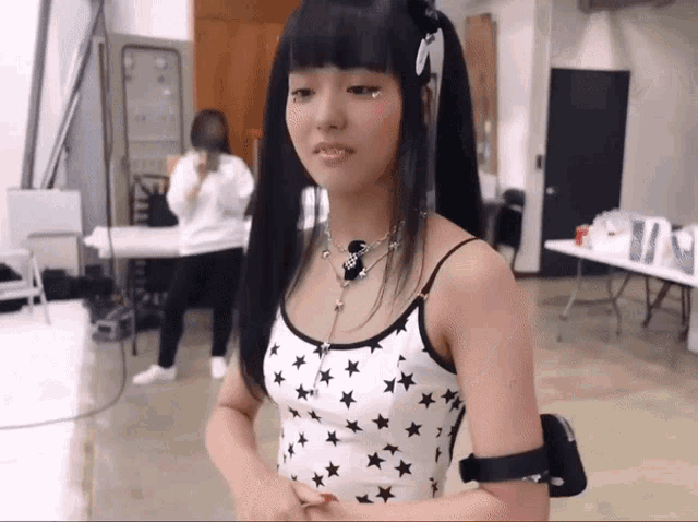 a girl wearing a white tank top with black stars and a necklace that says ' i love you ' on it