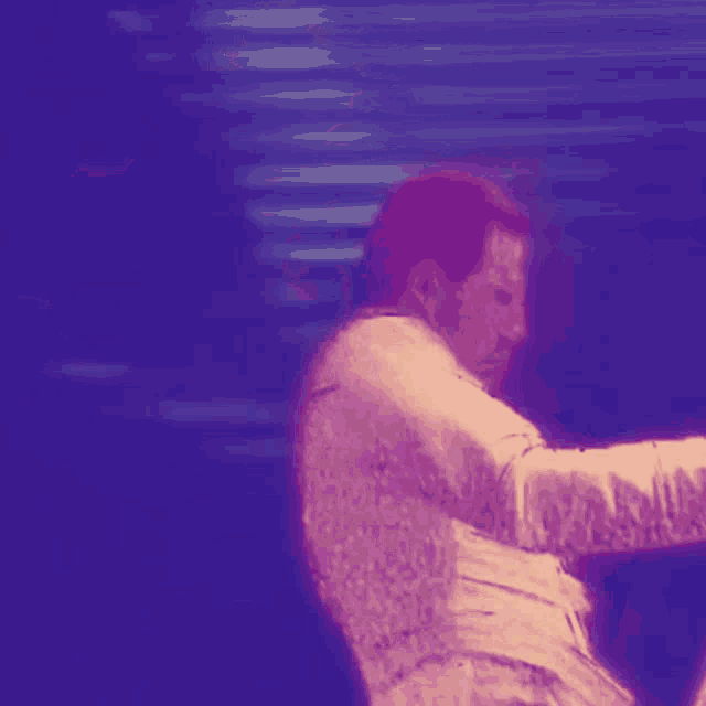 a man in a white shirt is standing in front of a microphone in a dark room .