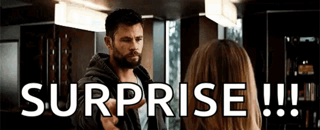 a man with a beard is standing next to a woman in a room and says surprise !!!