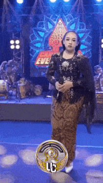 a woman is standing on a stage holding a microphone in front of a can eve sign .