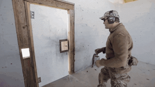 a man wearing ear defenders stands in front of a door that has a hole in it